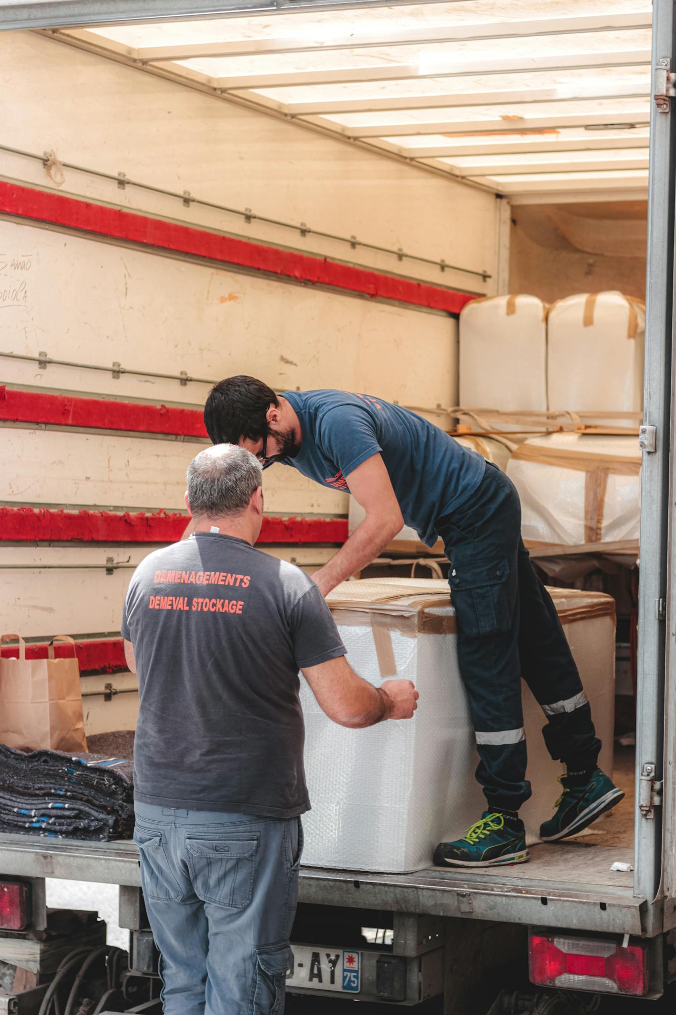 Two workers organizing cargo inside a delivery truck for shipping logistics.